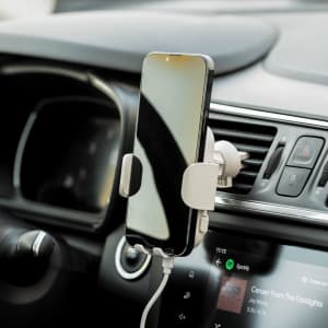 A wireless charger holder in white, mounted in a car, securely holding a smartphone near a dashboard display.