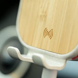 A wireless charger holder made of bamboo and white plastic, featuring a branding logo and wireless charging symbol.