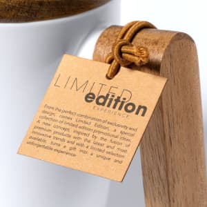 A white coffee mug with a wood handle and a tag attached. The mug features a branding logo.