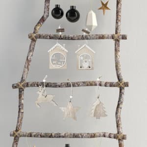 A decorative display of wooden Christmas ornaments, including stars, trees, and houses, on a rustic twig ladder.