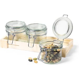 Three glass jars with metal clips, filled with assorted seeds, placed on a wooden tray.