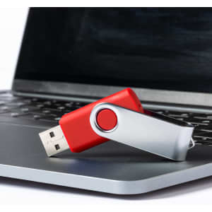 A red and silver USB memory drive resting on a laptop keyboard, featuring a swivel design and a logo.