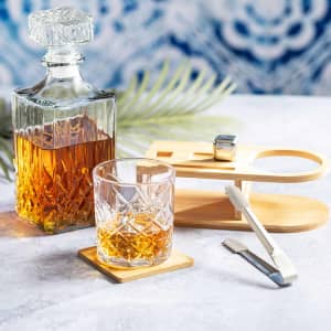 A drink bottle with a crystal design, a matching glass, bamboo coasters, and tongs, featuring amber whisky.