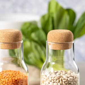 A drink bottle featuring a cork lid and a clear glass body, filled with orange lentils and white beans.