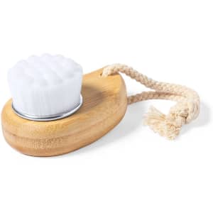 A face cleansing brush with a white bristle head and a bamboo handle, featuring a rope for hanging.