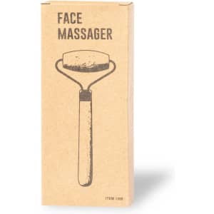 A rectangular box containing a face massager, featuring a wooden handle and a rounded stone head. The box has a simple design and logo.
