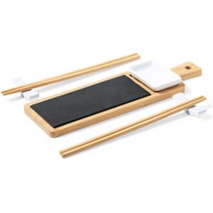 A bamboo sushi set featuring a black serving board, white sauce dish, and two wooden chopsticks.