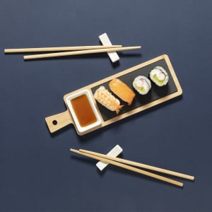 A wooden sushi serving set featuring various sushi pieces, a small bowl of soy sauce, and chopsticks on a dark surface.
