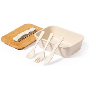 A cream-coloured container with a bamboo lid, accompanied by biodegradable cutlery: a knife, fork, and spoon.