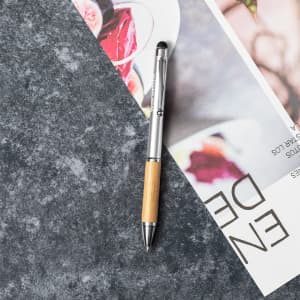 A silver and bamboo stylus touch ball pen rests on a grey marble surface next to a magazine.