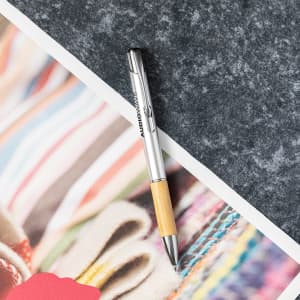 A silver and bamboo pen on a textured grey surface, alongside colourful patterned paper.