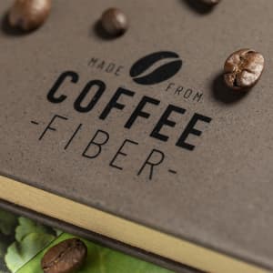 A notepad with a textured brown cover, featuring coffee beans scattered around and a logo.