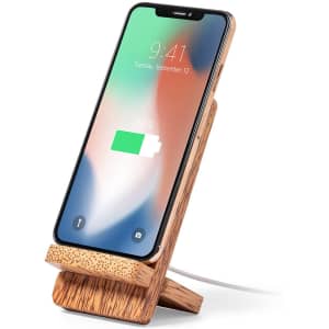 A wooden wireless charger with a phone propped up, displaying a battery charging symbol.