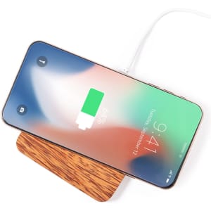 A wireless charger with a wooden base and a smartphone displaying a battery charge indicator.