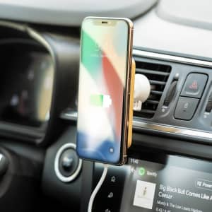 A wireless charger holder in a car, holding a smartphone that displays a charging icon. The holder is white.