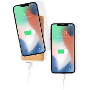 A cork-coloured power bank with two smartphones charging wirelessly, displaying battery status on the screens.