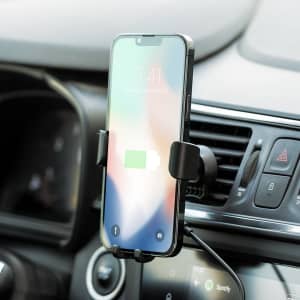 A car phone holder in black securely gripping a smartphone, mounted on a vehicle dashboard near air vents.