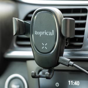 A black car phone holder mounted on a dashboard vent, featuring a branding logo and a charging cable attached.