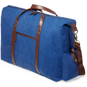 A large blue tote bag with brown leather straps and a front zip pocket. It features a side pocket and a logo.