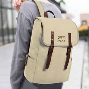 A beige backpack with brown straps and a logo, being worn on a person’s back outdoors.