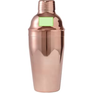 A cocktail shaker in a shiny rose gold finish with a lid and a branding label on the front.