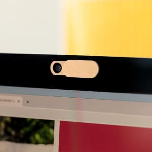 A beige webcam cover placed on the top of a computer monitor, partially covering the camera.