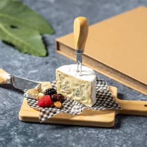 A cheese knife set featuring wooden handles and a small cheese board with blue cheese and mixed berries.