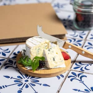 A cheese knife set with a wooden handle, featuring a knife and a round cheese on a bamboo board, against a decorative backdrop.