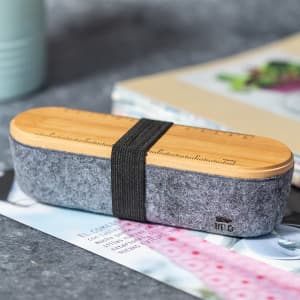 A grey felt pencil case with a bamboo lid and a ruler on top, secured with a black elastic band.