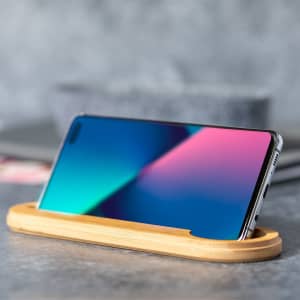 A smartphone displayed on a sleek bamboo stand, featuring a vibrant screen with blue and pink hues.