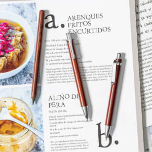 A set of wooden pens in varying shades of brown rests on a page of text and images, featuring a logo.