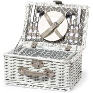 A white wicker picnic basket with a patterned interior, containing plates, cutlery, and a strap for securing items.