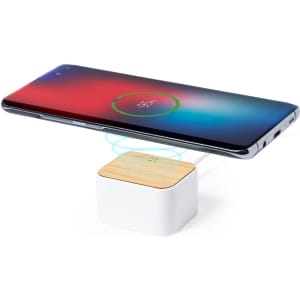 A wireless charging pad with a wooden top, placed beneath a smartphone displaying a charging indicator.