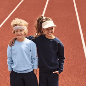 A blue sweatshirt and a navy sweatshirt worn by two children on a running track, one wearing a visor.