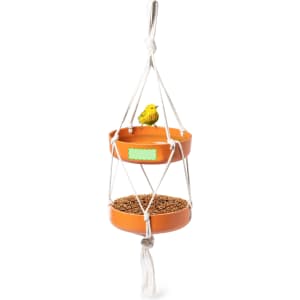 A hanging bird feeder with two terracotta bowls, featuring a yellow decorative bird on top and filled with seeds.