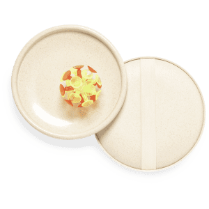 A round, beige game board with a colourful ball featuring orange and yellow pieces inside. It includes a lid.