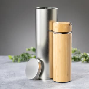 A bamboo drink bottle next to a silver cylindrical container, with green foliage in the background.