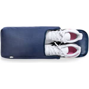 A navy shoe bag containing a pair of white sneakers with pink accents, featuring a logo on the side.