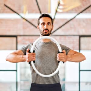 A man holds a circular, white exercise ring with black grips, set against a brick wall background.