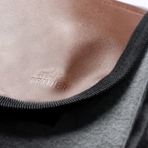 A grey picnic blanket with a brown leather accent and a textured border, featuring a logo.