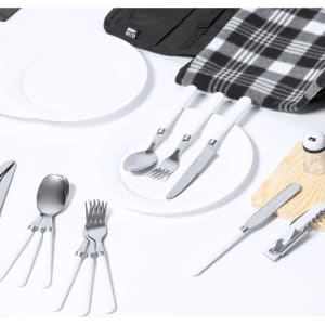 A black picnic backpack laid open reveals cutlery, plates, a checkered blanket, and a wooden serving board.