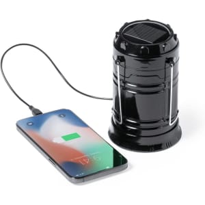 A black power bank lamp with a solar panel, connected to a smartphone for charging.