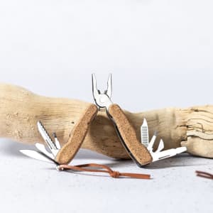 A multitool with pliers and various tools, featuring a cork handle, positioned on a piece of driftwood.