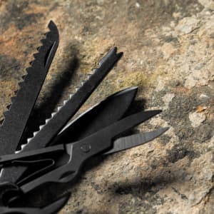 A multifunction pocket knife with black tools, including scissors and various blades, displayed on a textured surface.