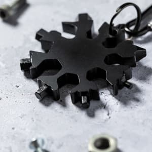 A black snowflake-shaped multitool with various functional features, surrounded by metallic hardware on a stone surface.