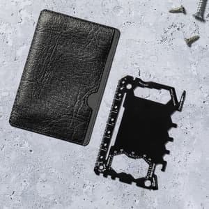A black multitool card next to a black wallet on a textured surface, with a few screws in the background.