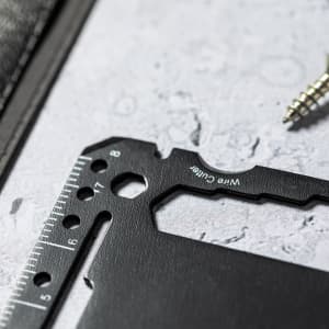 A black multitool featuring a wire cutter, ruler, and various measurement markings, resting on a textured surface.