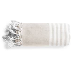 A rolled towel in beige with white stripes and tassels on one end, featuring a logo.