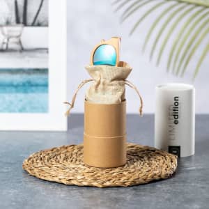 A pair of turquoise sunglasses is presented in a natural fibre pouch, housed in a cylindrical cardboard box.