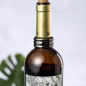 A brown wine bottle with a cork stopper and a decorative label, featuring a logo at the neck.